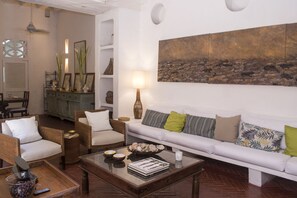 Un salon avec un canapé blanc, des fauteuils en osier, une table basse et un tableau accroché au mur.