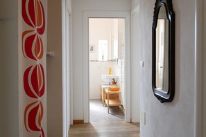 Un pasillo con un espejo, una puerta con diseño rojo y blanco y vista a una habitación con un lavabo y muebles de madera.