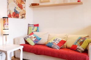Una sala de estar con un sofá color beige, cojines de colores, una mesa blanca y un cuadro en la pared.
