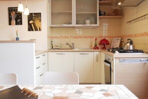 Une cuisine compacte avec des meubles blancs, un évier, une cuisinière et un coin repas comprenant une table et des chaises.