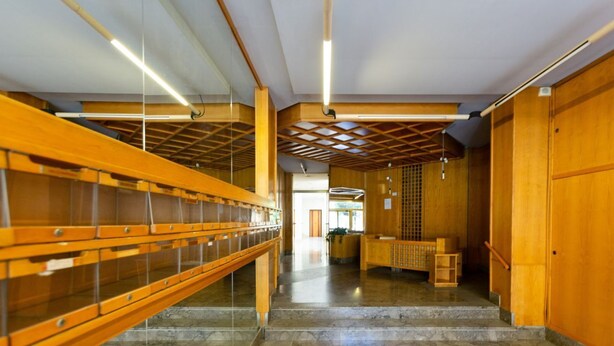 A hallway with wooden shelving units, a reception desk, and a staircase leading to an upper level.