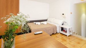 A hotel room with a wooden bed, a bedside table with a remote control, a white nightstand, and a vase with flowers.