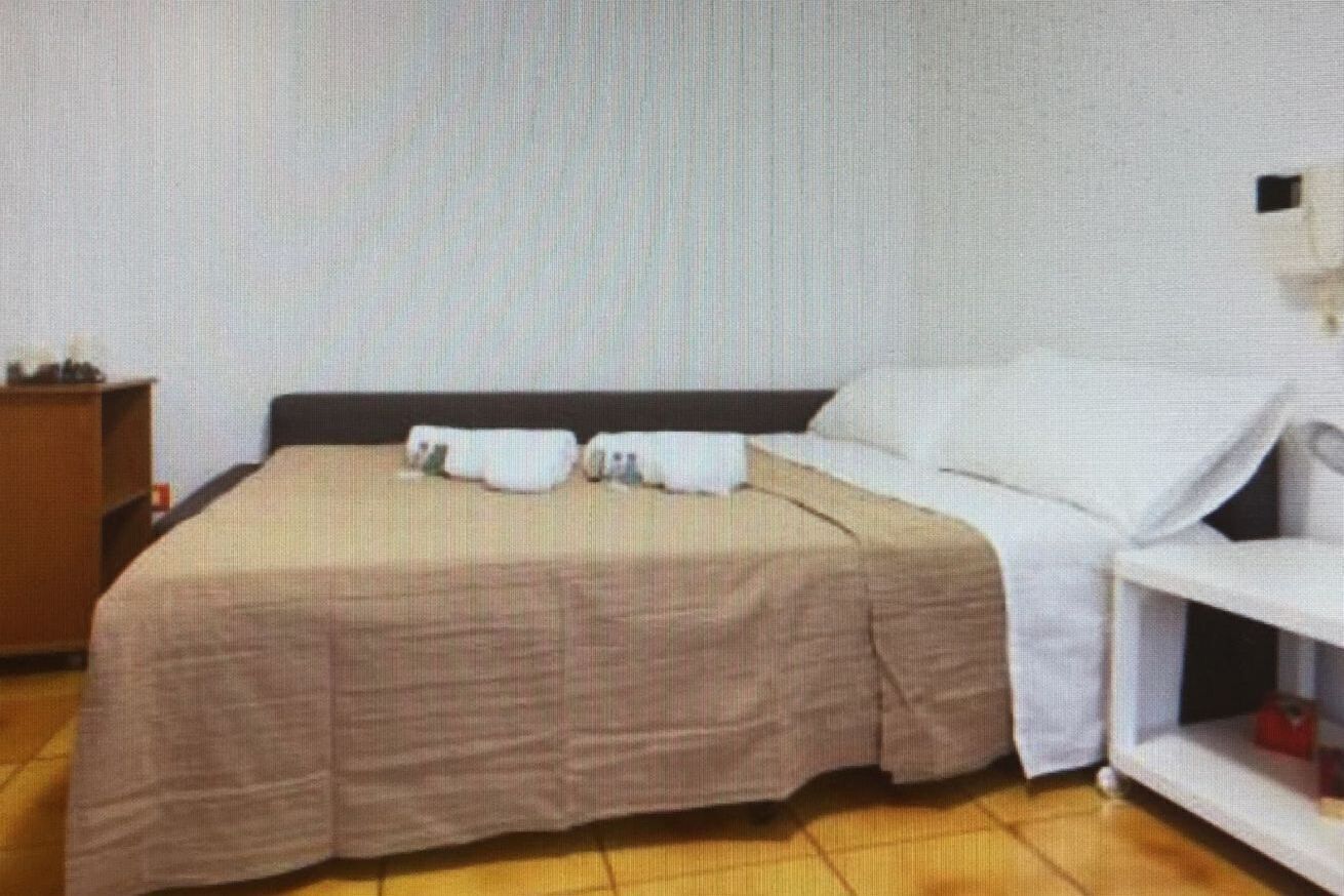 A hotel room with a bed, a nightstand, and a white wall.