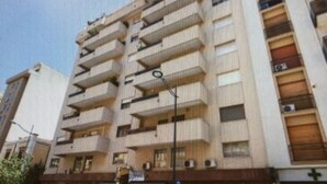 A multi-story building with balconies, a visible parking sign, and a cross symbol indicating a medical facility.