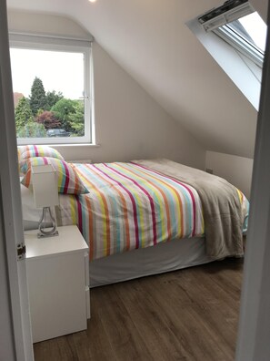 Cozy bedroom with a single bed, bedside table, and window offering a view of the outdoors.