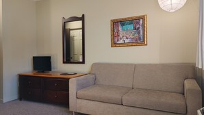 Una sala de estar con un sofá color beige, un aparador de madera, un televisor de pantalla plana, un espejo y un cuadro enmarcado.