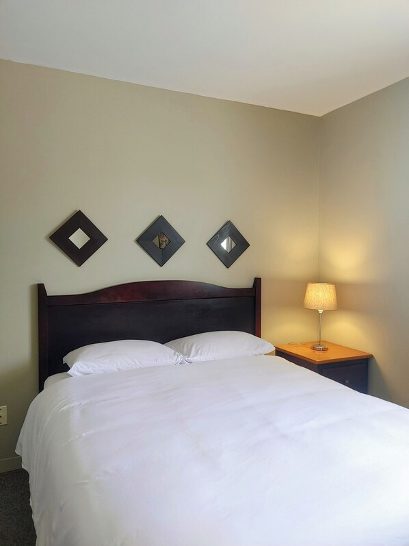 A neatly made bed with white linens, a dark wooden headboard, and a bedside table with a lamp. There are three wall-mounted square mirrors above the bed. - Hotel Le Must (Saint-Marc-des-Carrières)