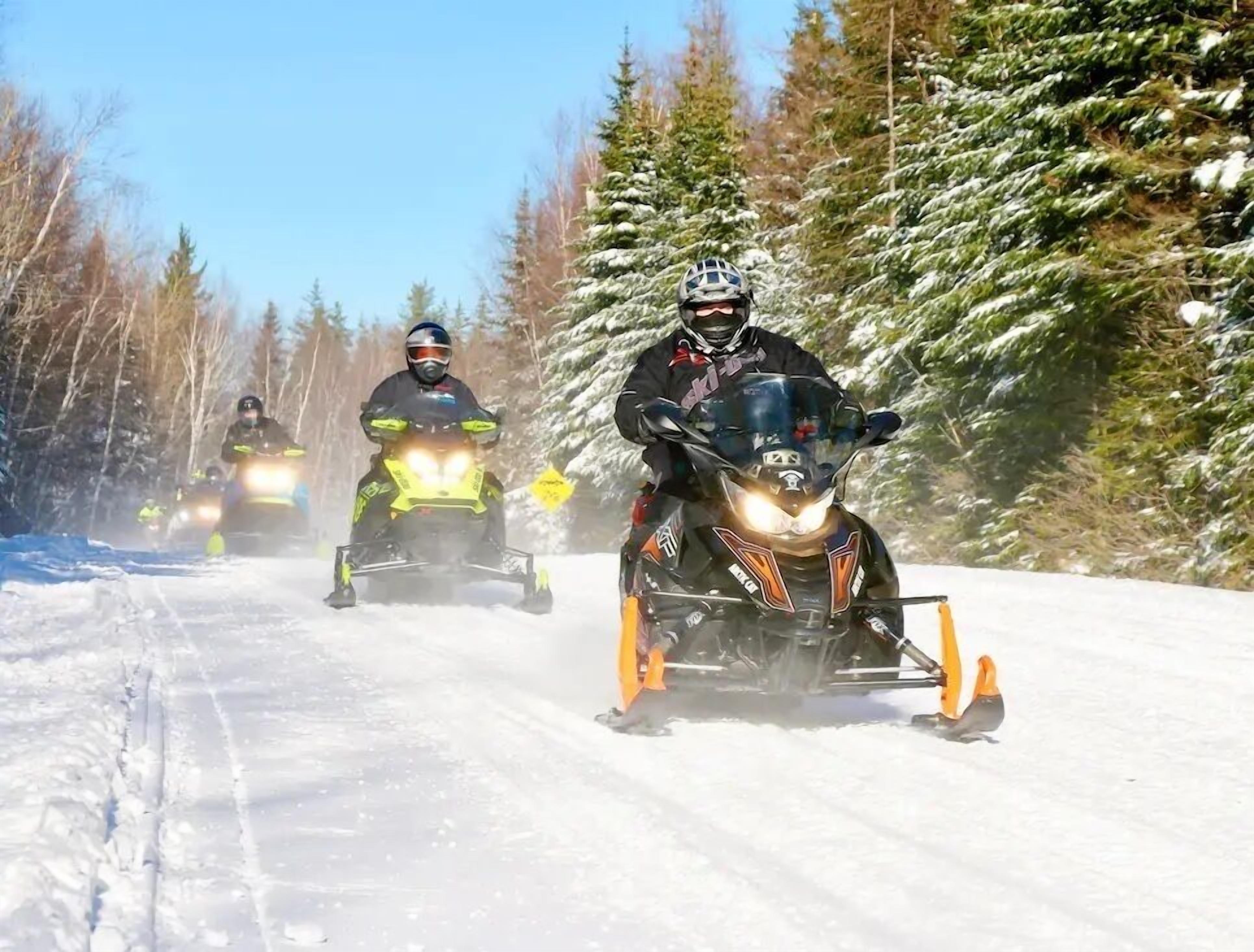 Three snowmobiles on a snowy road with trees on the sides.
