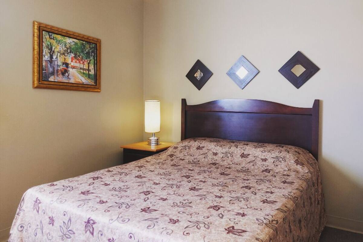 Ein Hotelzimmer mit Bett, Nachttisch, Lampe und einem Gemälde an der Wand.
