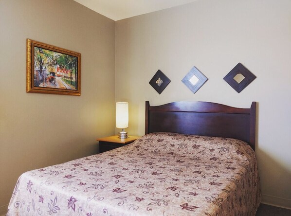 A hotel room with a bed, a nightstand, a lamp, and a painting on the wall. - Hotel Le Must (Saint-Marc-des-Carrières)