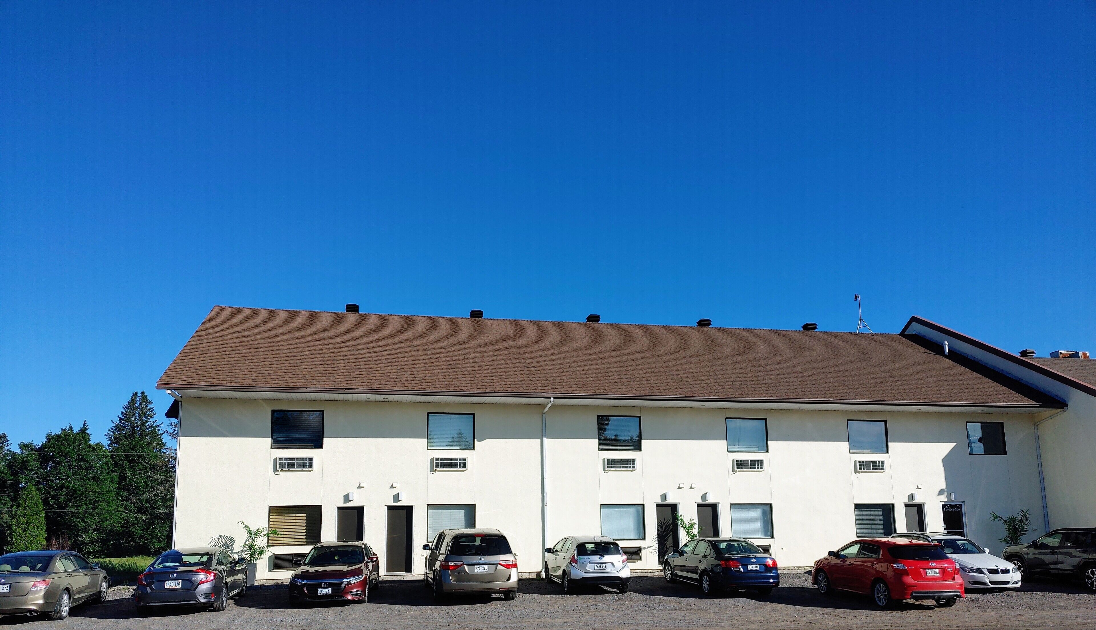 A multi-story building with a flat roof and several windows. There are multiple cars parked in front.