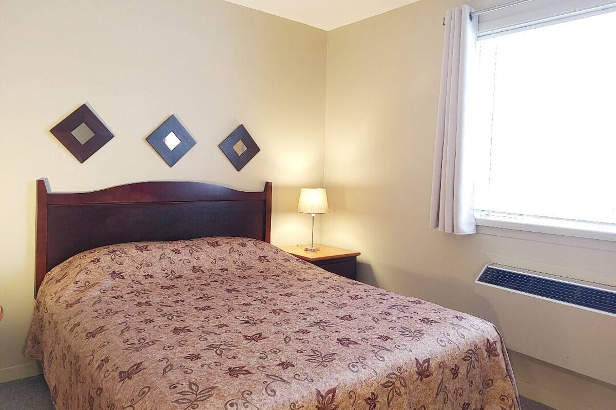 Ein Hotelzimmer mit einem Bett, einem Nachttisch mit Lampe und drei an der Wand befestigten, quadratischen Spiegeln.