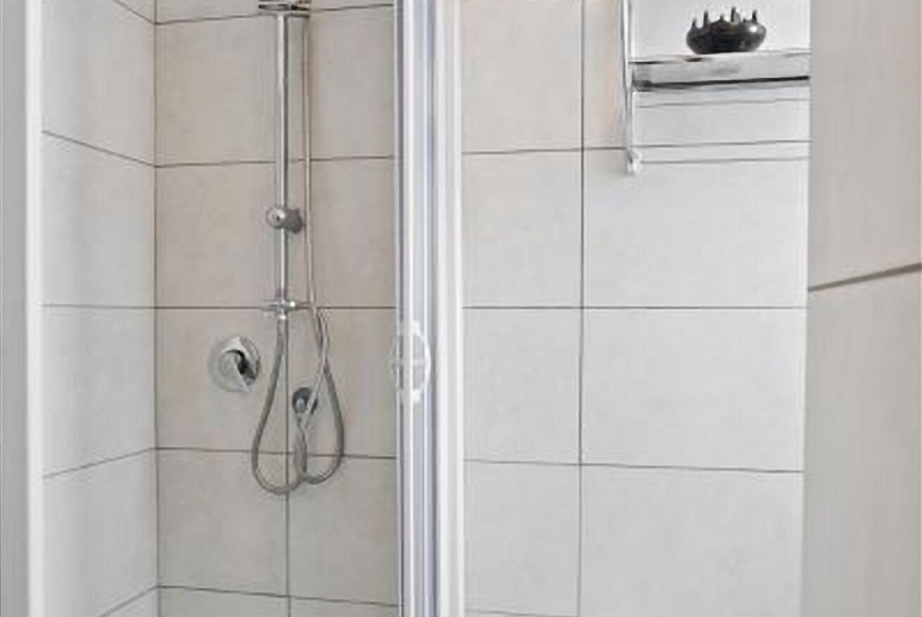 A glass-enclosed shower with a handheld showerhead and a wall-mounted faucet.