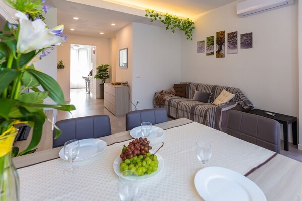 A dining area with a table set for four, a sofa, and a kitchen in the background. - GuestHost - NEW! Apartment X6 with WIFI, A/C, underground M1! (Milano)
