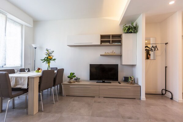 Una sala de estar moderna con comedor, televisor de pantalla plana y estanterías empotradas.