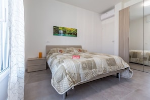 A bedroom with a bed, a nightstand, a mirror, and a picture on the wall. - GuestHost - NEW! Apartment X6 with WIFI, A/C, underground M1! (Milano)