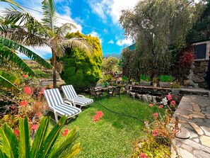 A well-maintained garden with a lawn, two striped lounge chairs, a stone pathway, and various plants and trees. - West cost of La Palma, views and tranquility (La Punta)