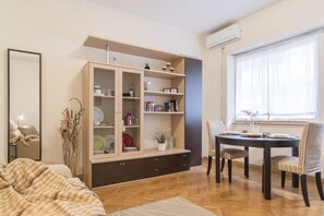 A room with a wooden cabinet, a dining table with chairs, a window with curtains, and a mirror.