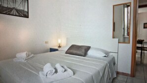 Een hotelkamer met een bed, nachtkastje, lamp, spiegel en een schilderij aan de muur.