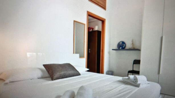 Een hotelkamer met een bed, een houten deur, een klein plankje en een stoel.