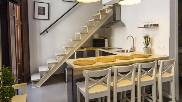 Eine moderne Küche mit einer zentralen Kochinsel, weißen Stühlen und einer Treppe zu einer oberen Ebene.