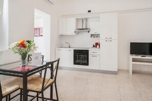 Una cocina moderna con armarios blancos, horno integrado y un televisor sobre un mueble.