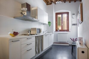 Una cocina con armarios blancos, una campana extractora de acero inoxidable, un ventanal con contraventanas y un radiador.