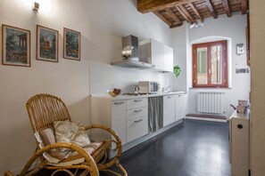 A kitchen with white cabinets, a wicker chair, and a window with shutters.