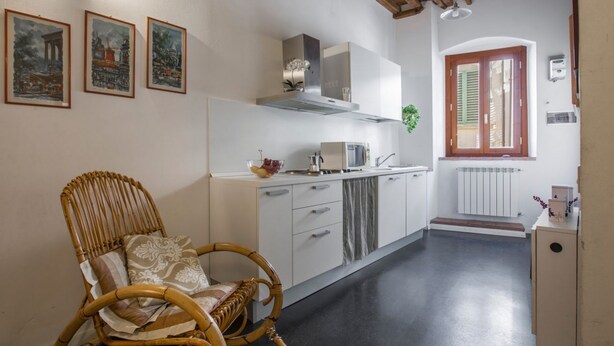 A kitchen with white cabinets, a wicker chair, and a window with shutters. - GuestHost - 55 sqm apartment for 4 people, located on the 1st floor (no elevator) of a historic building in the lively San Lorenzo district of Florence. Just a short distance from the famous market and the station, with a view of the Basilica of San Lore (Firenze)