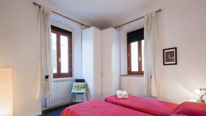 A room with two beds, a radiator, a chair, and a window with curtains. - GuestHost - 55 sqm apartment for 4 people, located on the 1st floor (no elevator) of a historic building in the lively San Lorenzo district of Florence. Just a short distance from the famous market and the station, with a view of the Basilica of San Lore (Firenze)
