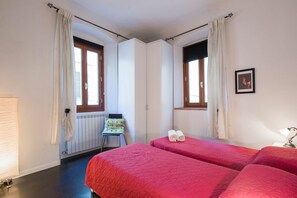 A room with two beds, a radiator, a chair, and a window with curtains.