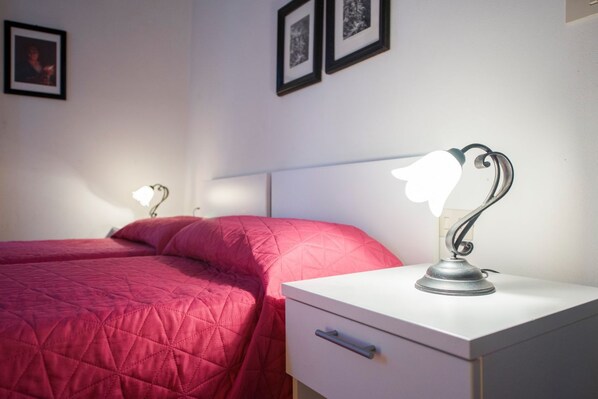 Un dormitorio con dos camas, una mesita de noche con lámpara y cuadros en la pared.