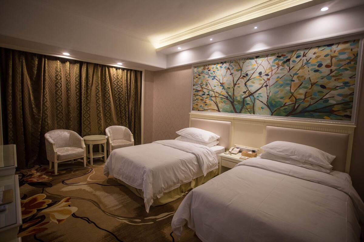 Een hotelkamer met twee bedden, een stoel, een klein tafeltje en een schilderij aan de muur.