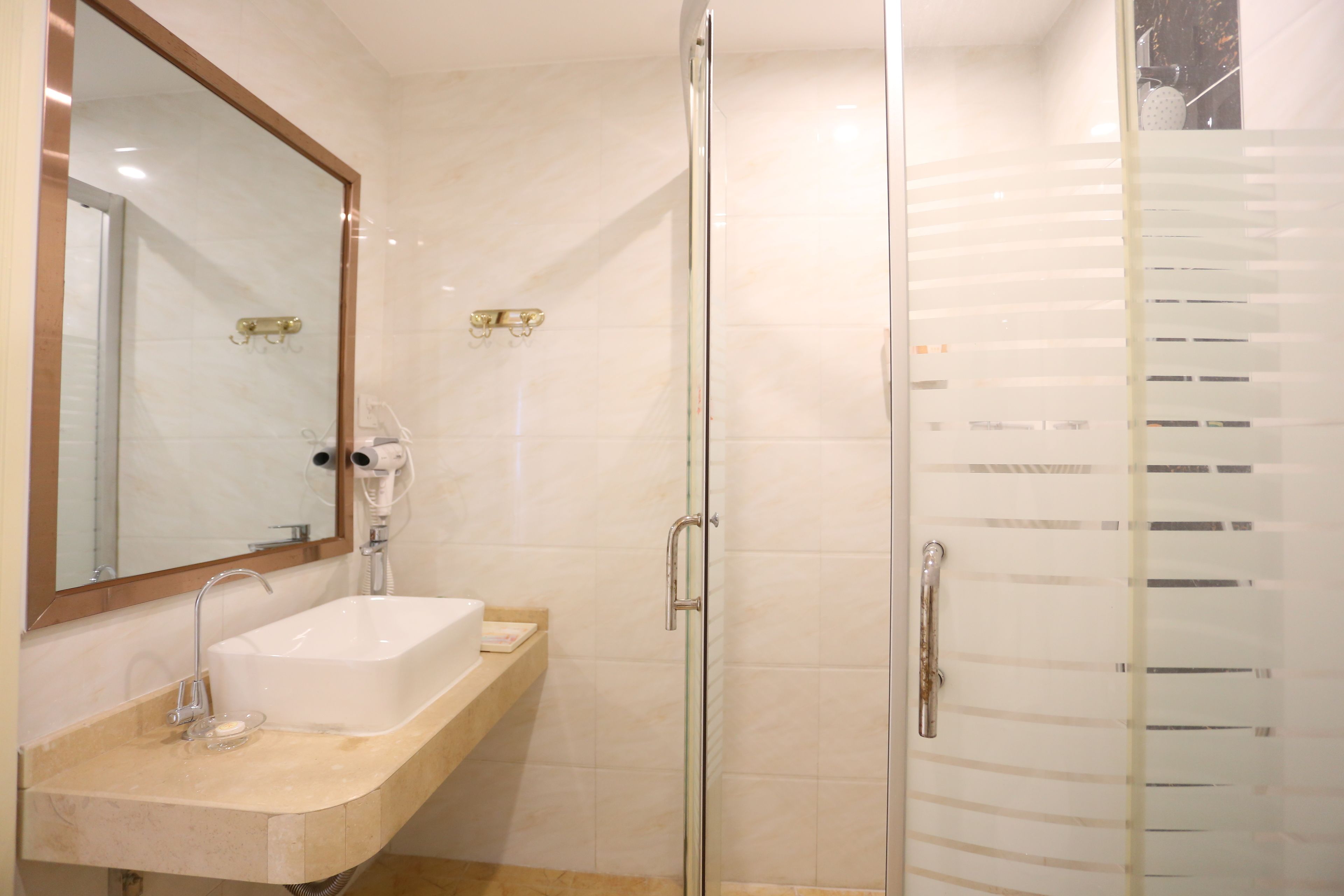 Un bany amb dutxa trencada per vidre, un lavabo blanc i un mirall sobre el lavabo.