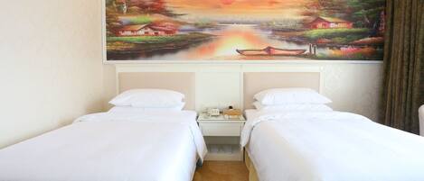 A hotel room with two beds, a painting of a sunset landscape on the wall, and a carpet with a floral design.