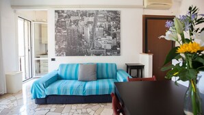 A room with a sofa, a dining table, a vase with flowers, and a cityscape painting on the wall. - GuestHost - NEW - Forlanini apartment for 4! (milano)