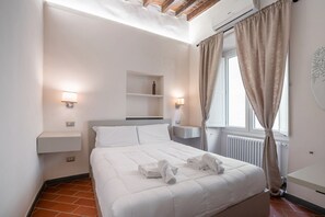 A hotel room with a bed, bedside lamps, a shelf, and a window with curtains.