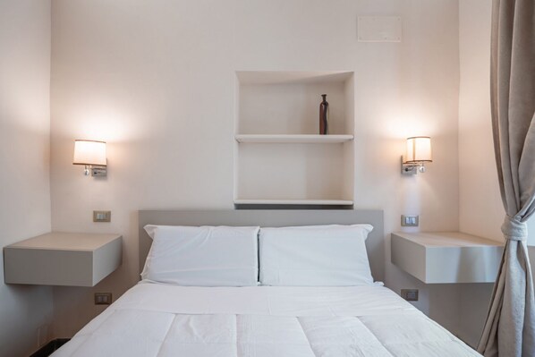 Een hotelkamer met een bed, twee nachtkastjes, een plank boven het bed en twee wandlampen.