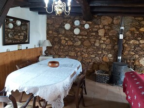 Un comedor con pared de piedra, una mesa de madera con mantel de encaje blanco y una estufa rústica.