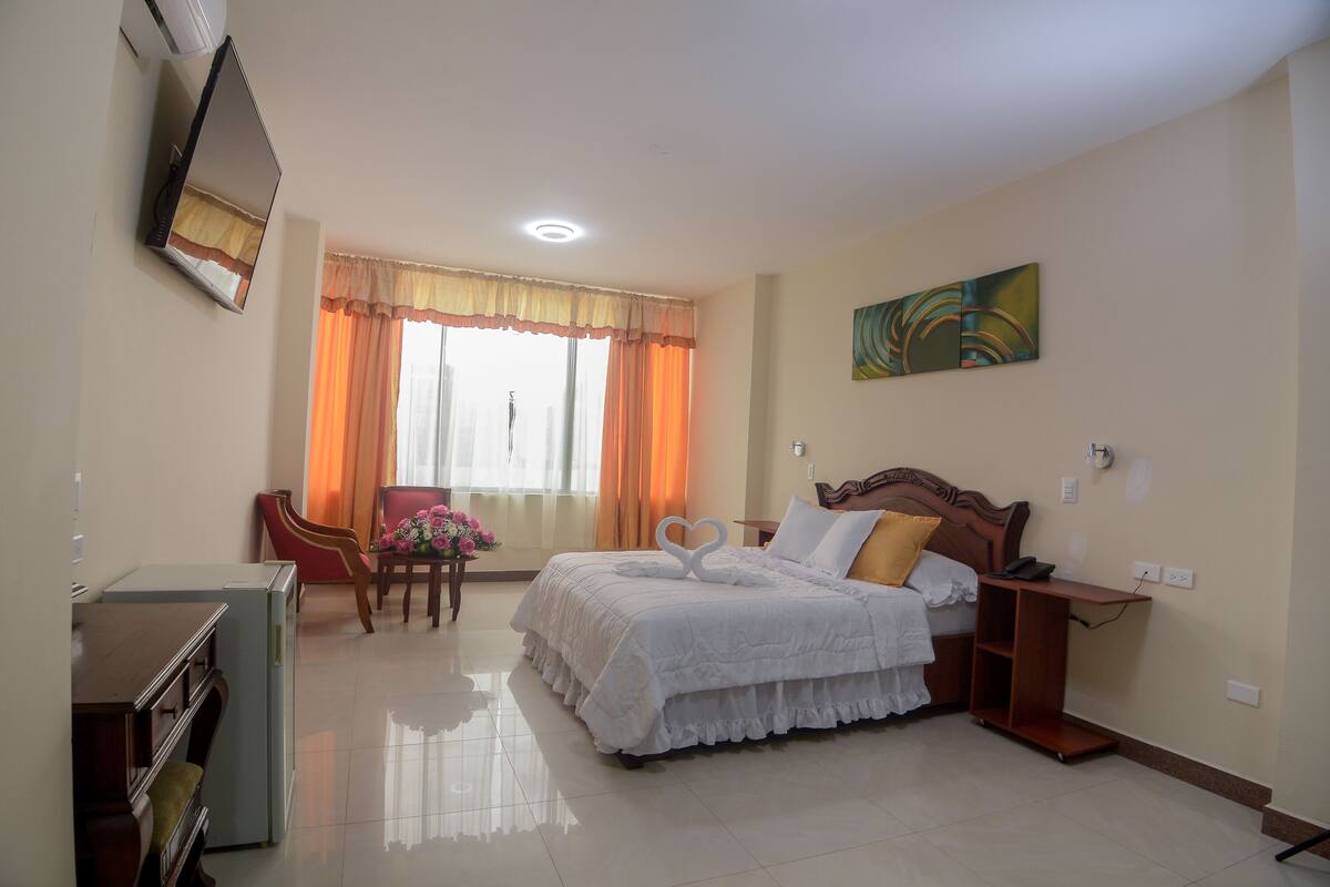 Una habitación de hotel con cama, escritorio, silla y ventana con cortinas.