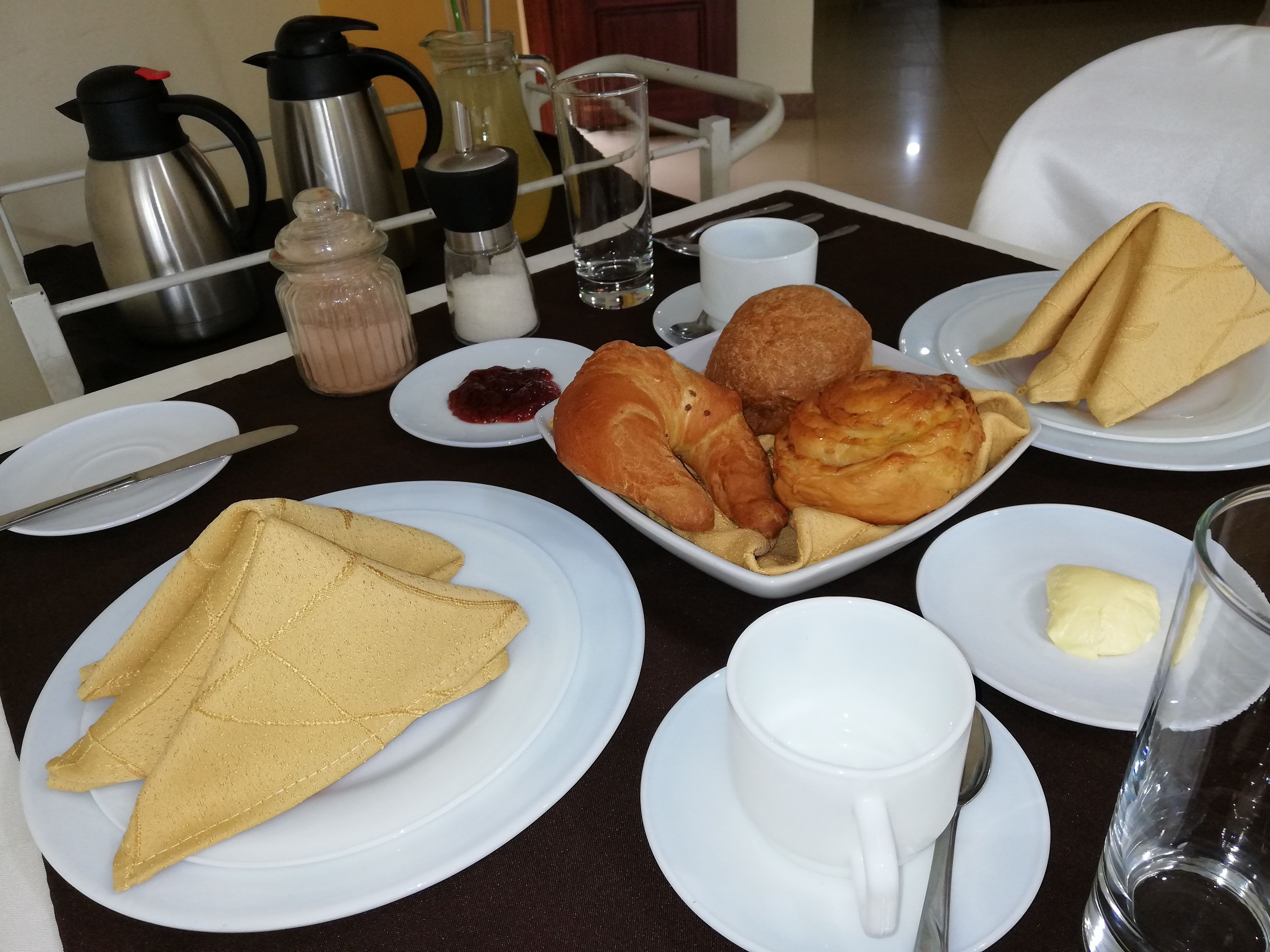 A breakfast table with croissants, a jug of milk, a cup of coffee, and a pitcher of juice.