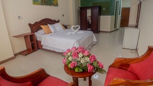 Habitación de hotel con cama, armario de madera, escritorio, sillón rojo y una mesa con un ramo de flores.
