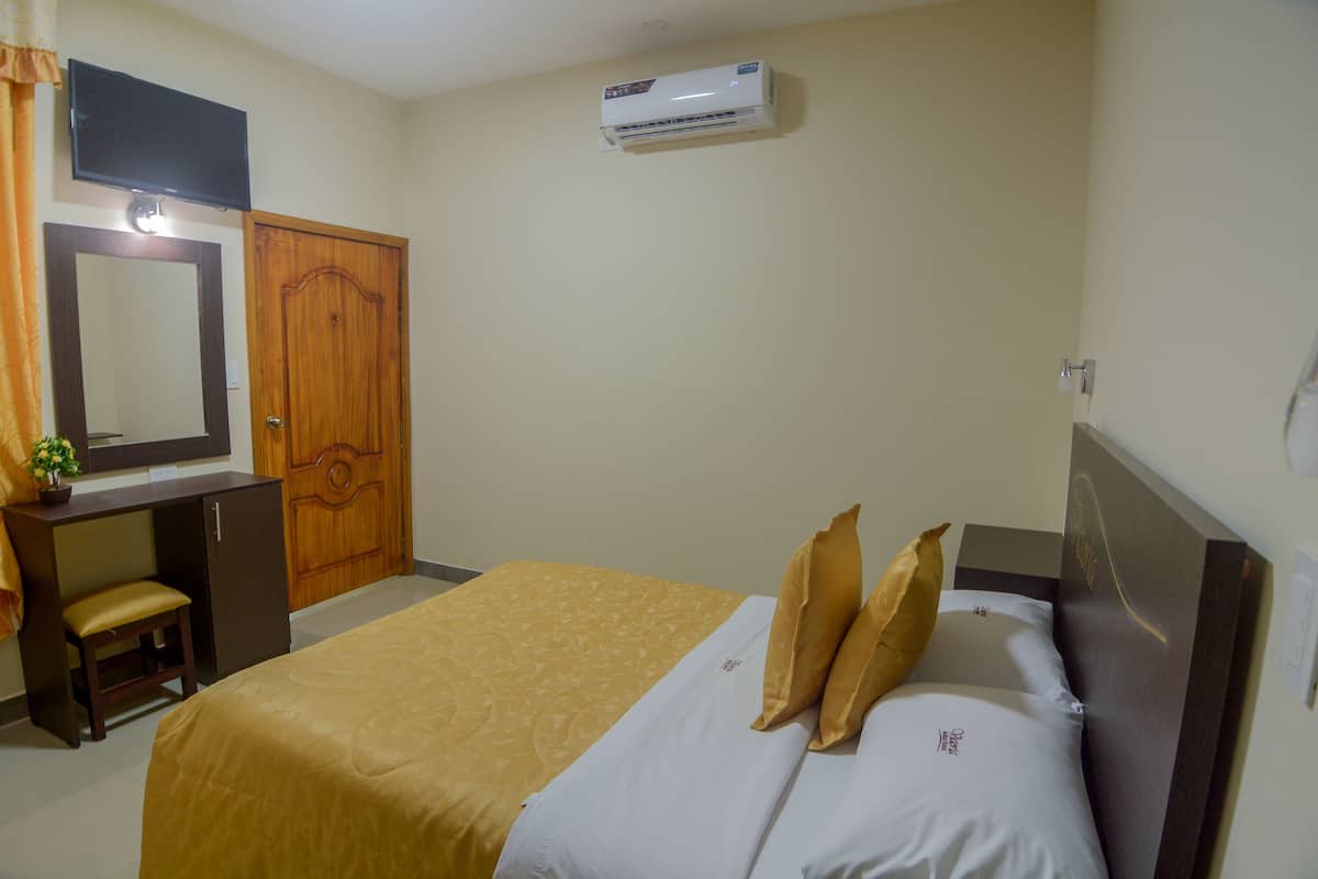 Habitación de hotel con cama, escritorio, silla, espejo y equipo de aire acondicionado.
