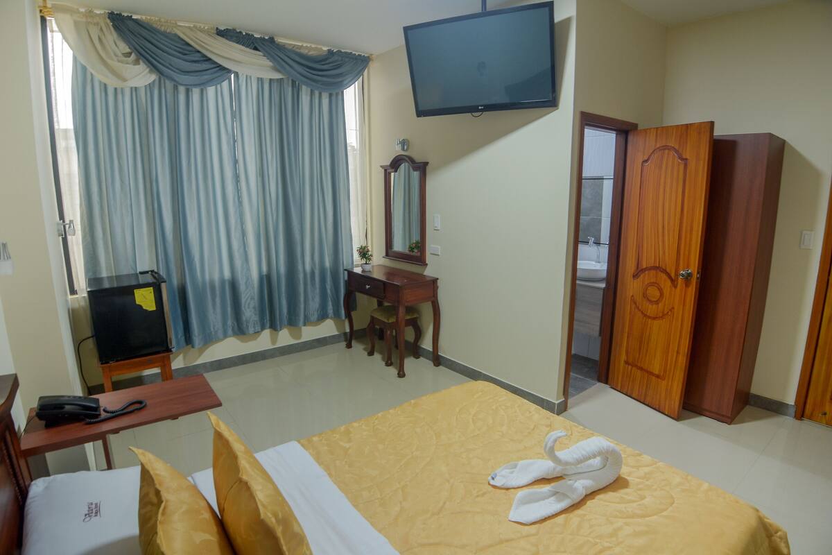 Habitación de hotel con cama, escritorio con teléfono, televisor montado en la pared, espejo y armario.