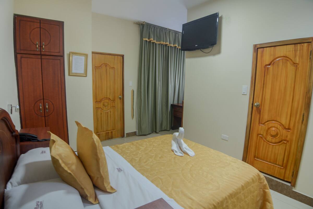 Una habitación de hotel con una cama, un armario de madera, un televisor montado en la pared y una cortina.