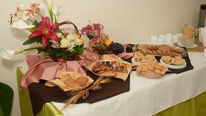 Una mesa de buffet con diversos alimentos, como pan, frutas y un arreglo floral.