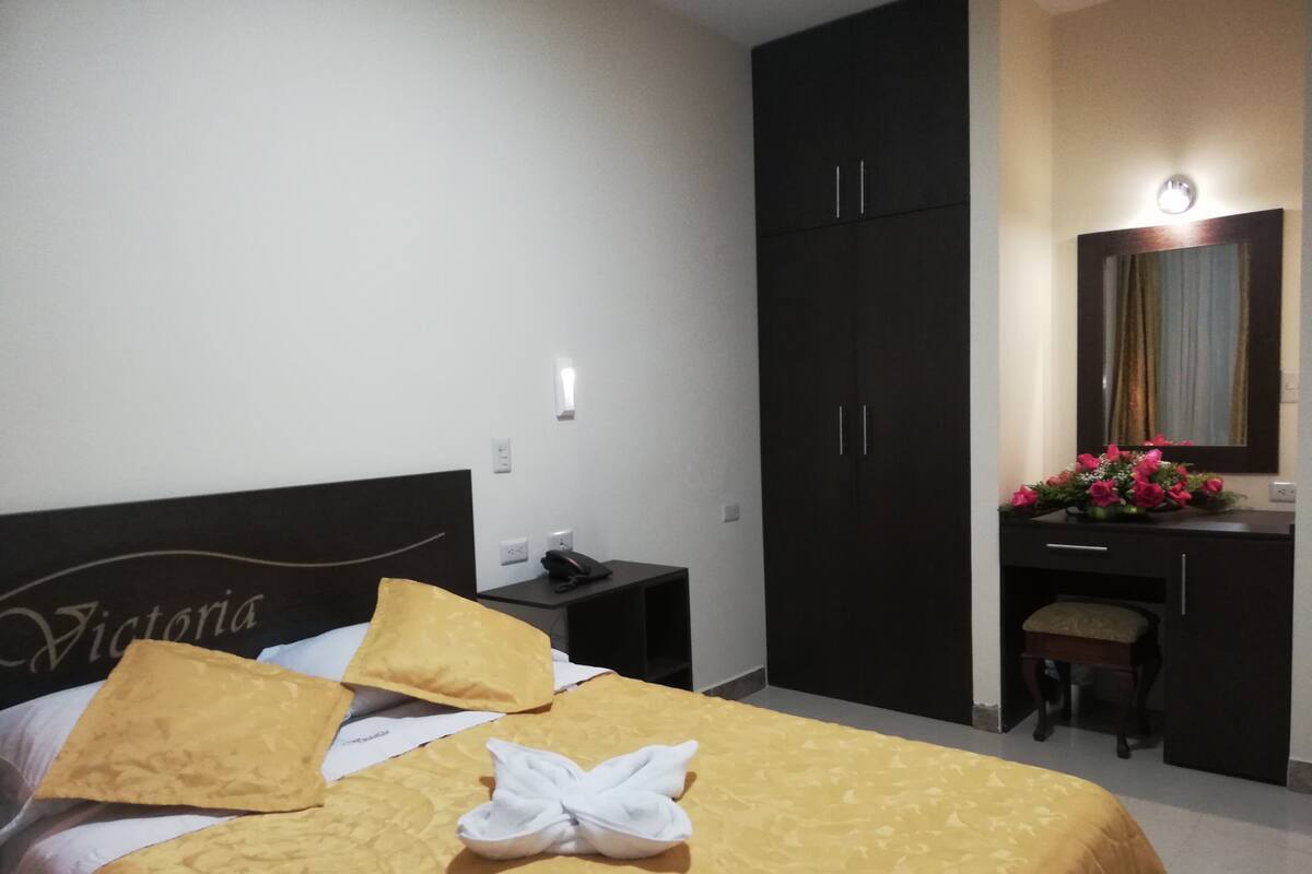 Una habitación de hotel con cama, escritorio, armario y espejo.