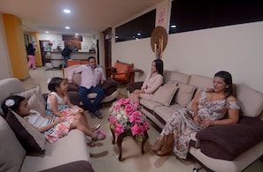 A living room with a reception desk, a coffee table with a floral arrangement, and a wall-mounted decorative item. - Victoria Suites Hostal (Santo Domingo de los Colorados)