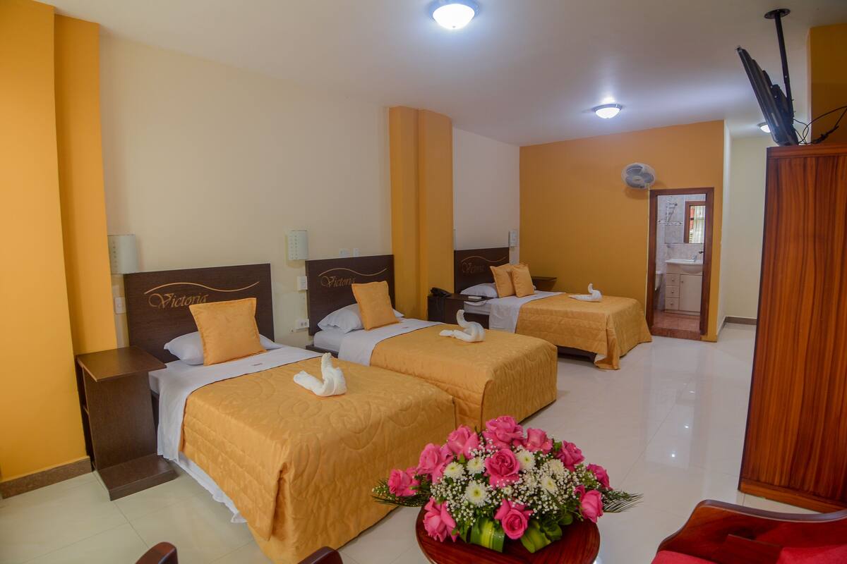 Habitación de hotel con tres camas, un armario de madera, un escritorio de madera y un arreglo floral.