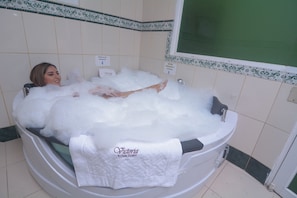 A bathtub filled with bubbles, a towel, and a sign indicating a 'Rion Desenque' and 'Rion Encender y Apagar' function. - Victoria Suites Hostal (Santo Domingo de los Colorados)